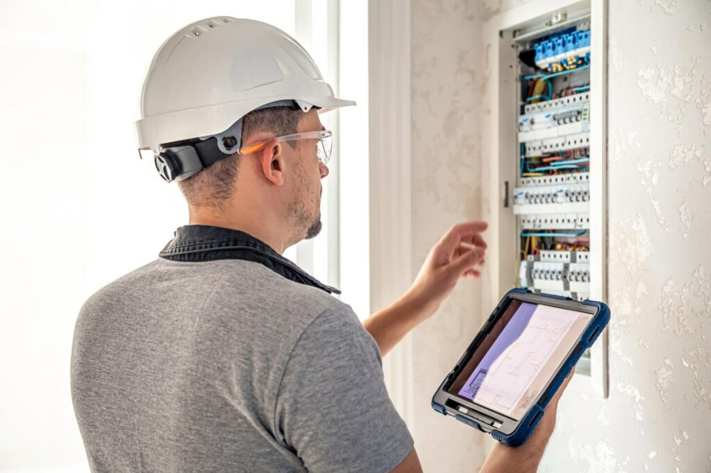 man electrical technician working switchboard with fuses uses tablet 169016 23722